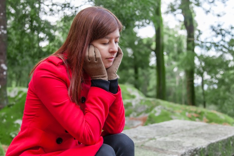 Young woman feeling depressed sitting on a stone table and bench